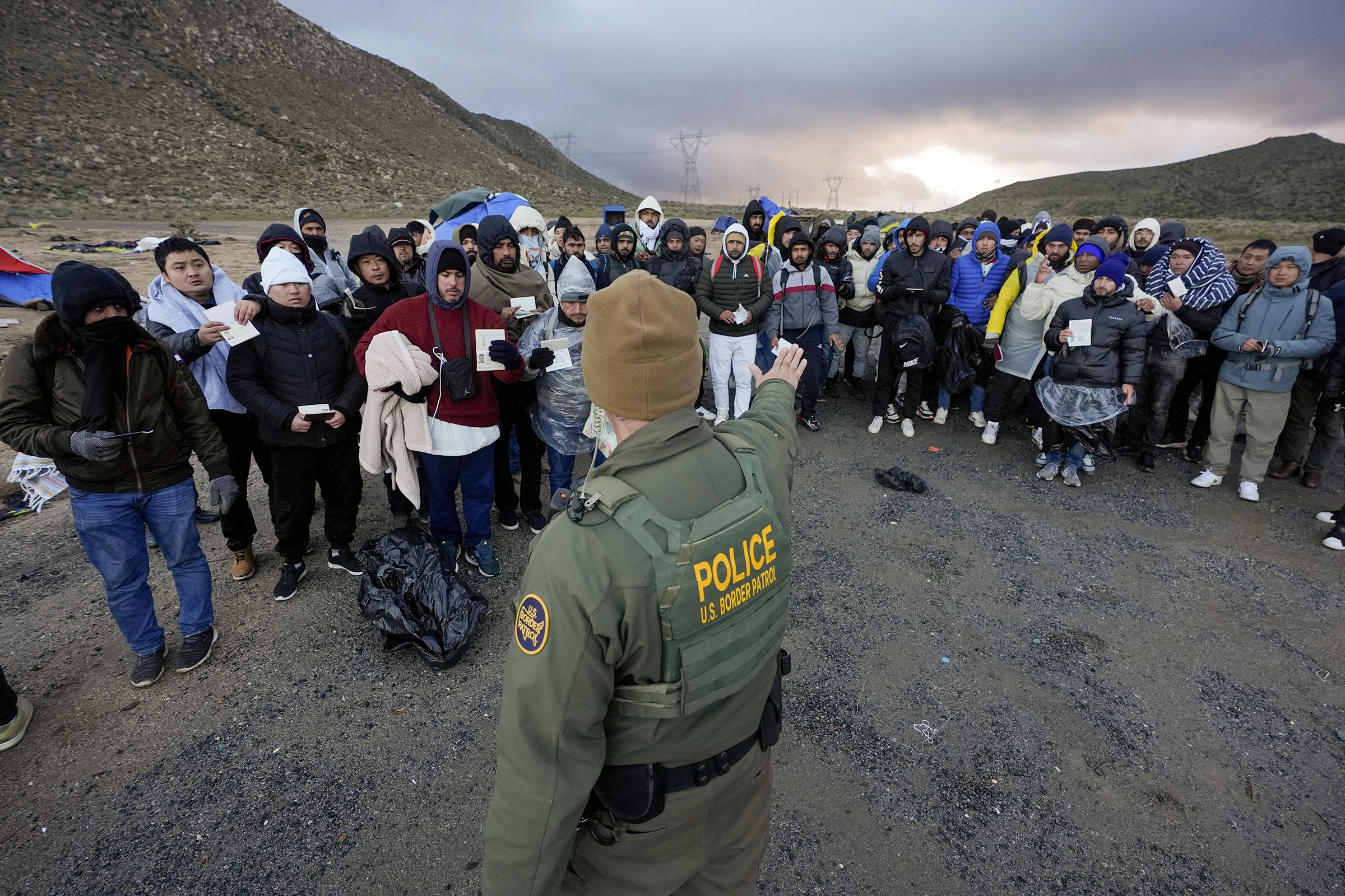 A Border Patrol agent asks asylum-seeking migrants to line up in a makeshift, mountainous campsite after the group crossed the border with Mexico, Friday, Feb. 2, 2024, near Jacumba Hot Springs, Calif. (AP Photo/Gregory Bull)