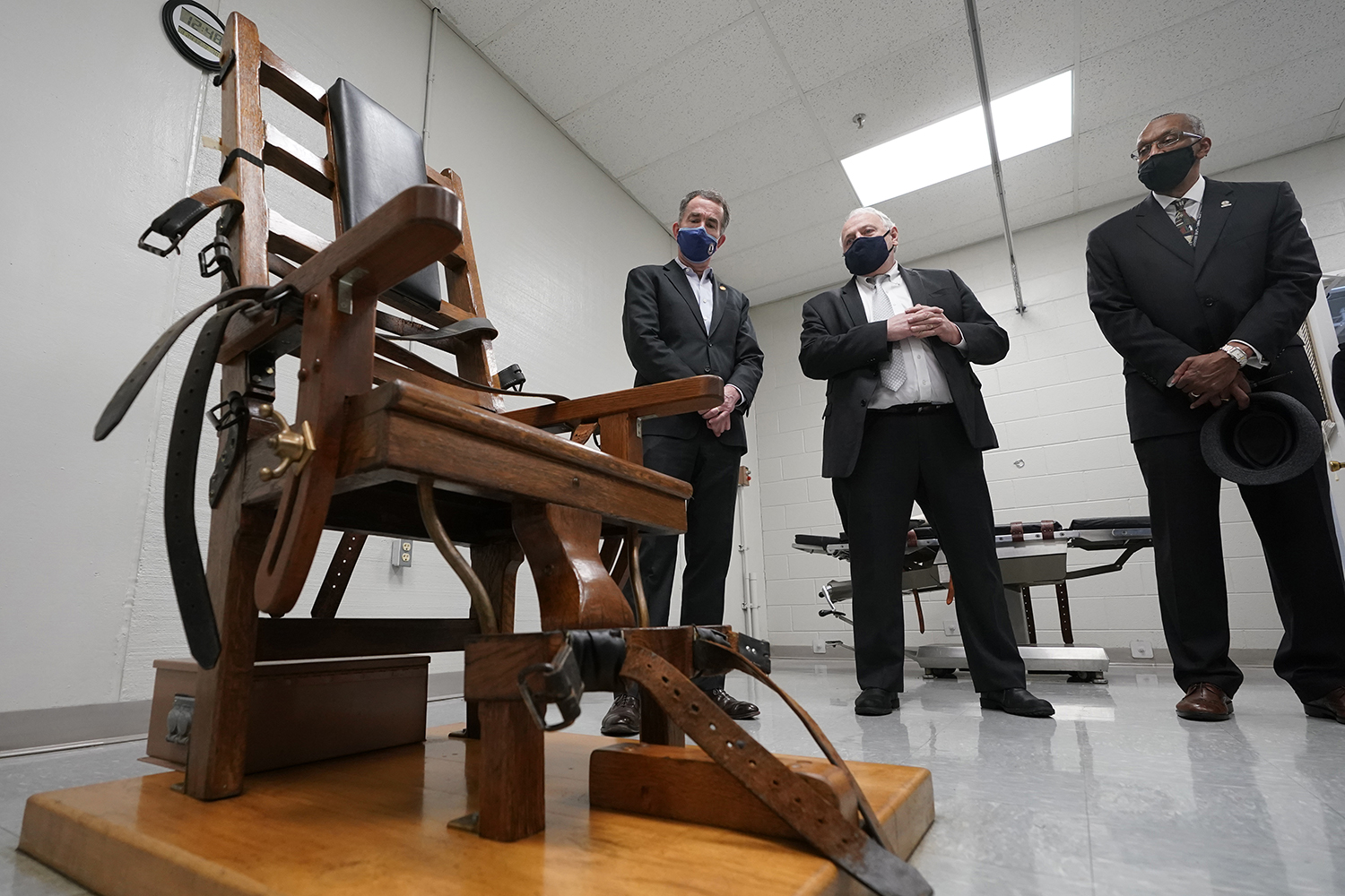 Virginia Gov. Ralph Northam, left, looks over the electric chair in the death chamber at Greensville Correctional Center with Operations Director George Hinkle, center, and Warden Larry Edmonds, right, prior to signing a bill on March 24, 2021, abolishing the death penalty in the state. (AP Photo/Steve Helber)