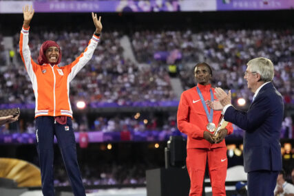 Women's marathon gold medalist Sifan Hassan, left, of the Netherlands, reacts as IOC President Thomas Bach prepares to present her medal during the 2024 Summer Olympics closing ceremony at the Stade de France, Sunday, Aug. 11, 2024, in Saint-Denis, France. (AP Photo/Ashley Landis)