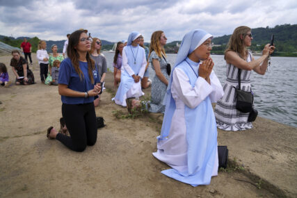 Sister Mary Fatima Pham, second from right, kneels with fellow Catholics as they watch the Eucharist brought on board a boat on the Ohio River at the Steubenville Marina in Steubenville, Ohio, Sunday, June 23, 2024. The National Eucharistic Pilgrimage will conclude at the National Eucharistic Congress in Indianapolis in mid-July, the first held in more than 80 years. (AP Photo/Jessie Wardarski)