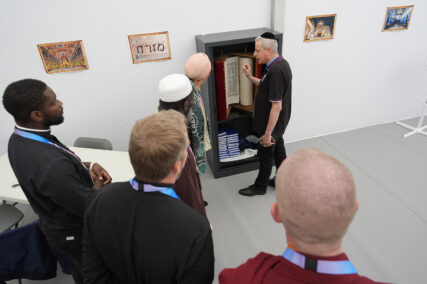 Rabbi Moshe Lewin, right, shows a Torah scroll to Muslim representative Najat Benali, with pink head covering, and to catholic priest Jason Nioka, left, in the inter-religious hall the Olympic Village at the 2024 Summer Olympics, Tuesday, July 23, 2024, in Paris, France. (AP Photo/Rebecca Blackwell)