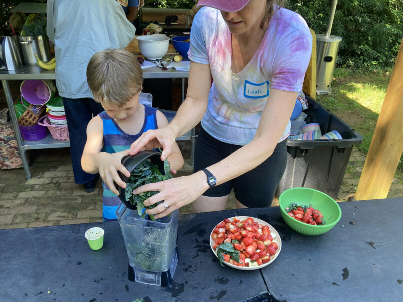 Grow It organizer Leah Reichardt-Osterkatz, right, helps children make smoothies from strawberries  they picked, plus kale grown on the farm, at Spring Forest in Hillsborough, North Carolina, on Wednesday, May 29, 2024. (RNS photo/Yonat Shimron)