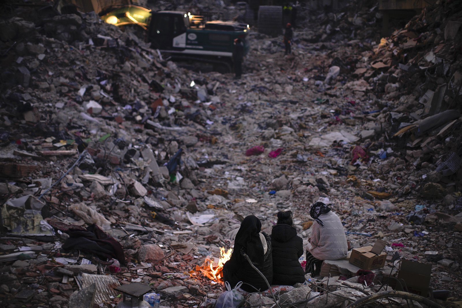 Members of a family keep warm next to a fire as they follow a rescue team searching for their relatives among destroyed buildings in Antakya, southern Turkey, Feb. 15, 2023. One month after a powerful quake devastated parts of Turkey and Syria, hundreds of thousands of people continue to have “extensive humanitarian needs,” including shelter and sanitation, a United Nations official said March 6, 2023. (AP Photo/Francisco Seco, File)