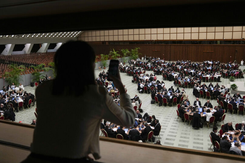 An individual takes a photo of the 16th General Assembly of the Synod of Bishops in the Paul VI Hall at the Vatican, Oct. 9, 2023. (AP Photo/Alessandra Tarantino)